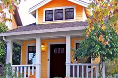 a yellow house with two pumpkins on the front porch