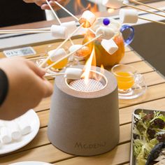 a person is lighting marshmallows on top of an outdoor fire pit while other people sit around the table