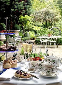 a table topped with plates and cups filled with food next to a cake stand full of desserts