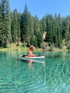 a person on a surfboard in the water near some trees and rocks with clear blue water