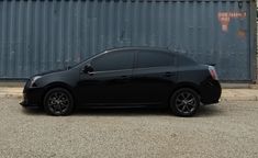 a small black car parked in front of a metal building with a sign on it