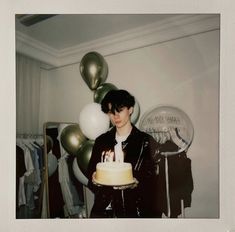 a woman holding a cake with candles on it in front of balloons and streamers