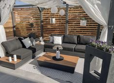 an outdoor living area with grey couches and white drapes on the side wall