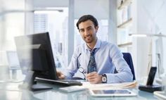 a man sitting at a desk in front of a laptop computer and holding a pen