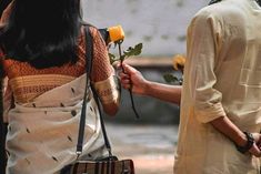 two people standing next to each other and one is holding a rose in her hand