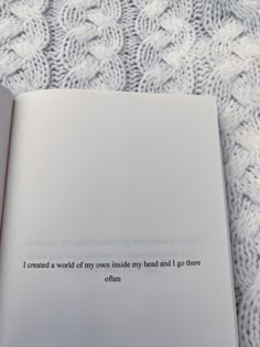 an open book sitting on top of a bed next to a white knitted blanket