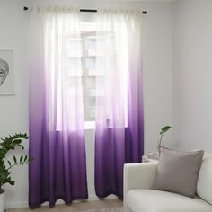 a living room with a white couch and purple ombreache curtains on the window