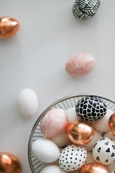 a basket filled with different colored eggs on top of a white table next to pink and gold balls