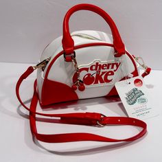 The Bag Is Made Of High-Quality Faux Leather And Nylon, With A Canvas Lining For Added Comfort. It Also Comes With A Bag Charm And Other Strap For Added Versatility. A Gorgeous White Exterior And Red Faux Leather Handles, This Bag Is Sure To Turn Heads. It Features A Zip Closure And An Adjustable Strap For Your Convenience. The Cherry Coke Pattern And London Theme Make This Bag A Must-Have For Any Coca-Cola Fan Or Collector. Retro White Satchel With Adjustable Strap, Retro White Shoulder Bag For School, White Retro Shoulder Bag For School, Retro Crossbody Satchel For Errands, Vintage White Bag For Errands, Retro White Bag For Everyday Use, White Retro Shoulder Bag For Everyday Use, Retro White Bags For Everyday Use, White Bags With Zipper Closure As Gift