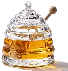 a glass honey pot with a wooden spoon in front of the lid on a white background