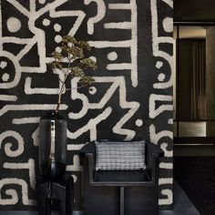 a black and white wall with a plant in a vase next to a small chair