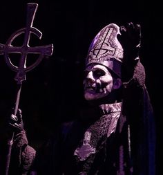 a creepy looking man holding a cross and wearing a purple mask on his face in the dark