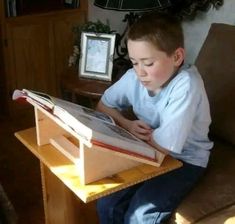 a young boy sitting on a couch reading a book with his eyes closed and looking at the pages