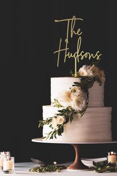 a white wedding cake with greenery and the words the hudsons on top