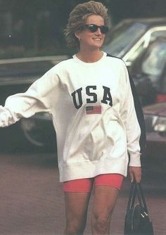 the woman is walking down the street with her hand in her pocket and wearing an american flag sweatshirt