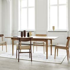 a dining room table and chairs in front of two large windows with white trim on the walls