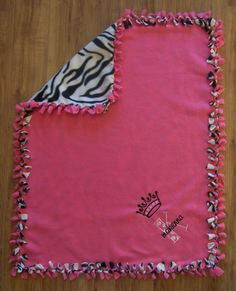 a pink and zebra print blanket on top of a wooden floor next to a black and white pillow