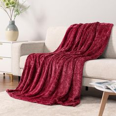 a couch with a red blanket on top of it next to a white table and vase