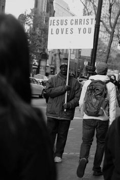 black and white photograph of people walking down the street with a sign that says jesus christ loves you