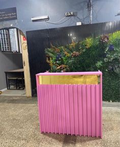 a pink trash can sitting on top of a floor next to a green plant wall