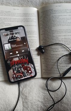 an open book with headphones on it next to a cell phone and earbuds