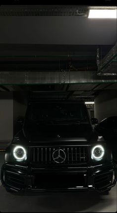 the front end of a black mercedes suv in a parking garage with its lights on