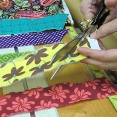 a person cutting fabric with scissors on a wooden table next to other fabrics and cloths