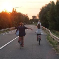 two people riding bikes down the road with their arms in the air