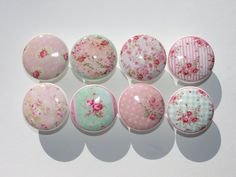 six pink and green flowered buttons on white surface with shadows from the back ground