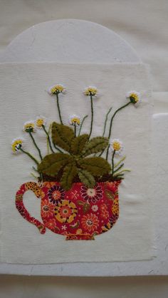 a red cup with flowers in it on a white cloth covered wall hanging ornament