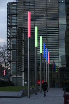 a person walking down a sidewalk next to tall metal poles with colored lights on them