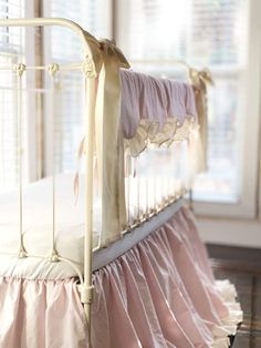 a white crib with pink ruffled bedspread on it's sides