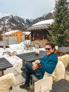 a man sitting at a table in the middle of a snow covered area with mountains in the background