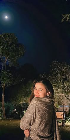 a woman standing in front of a bench at night with the moon shining behind her