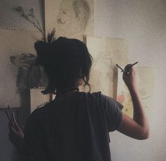 a woman is drawing on the wall with her pencils and some drawings behind her