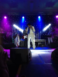 a man standing on top of a stage in front of purple and blue lights at night