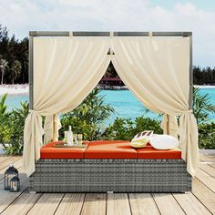 an outdoor day bed with drapes and pillows on the deck next to water, surrounded by palm trees