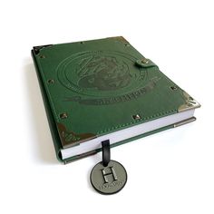 a green book with a metal disc attached to it's cover, sitting on top of a white surface