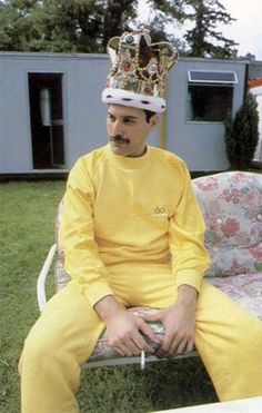 a man wearing a crown sitting on top of a chair in front of a house