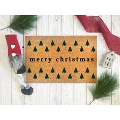 a merry christmas door mat with trees and gnomes on it next to red ribbon