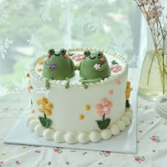 two green frogs sitting on top of a white cake