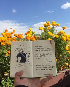 someone is holding up an open book in front of some yellow flowers and blue sky