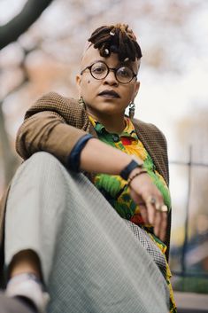 a woman sitting on the ground with her legs crossed and wearing eyeglasses, looking off to the side