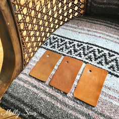 three leather tags sitting on top of a wooden chair next to a woven seat cushion