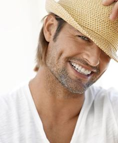 a man wearing a straw hat smiling at the camera with his hand on his head