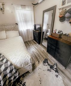 a bed room with a neatly made bed next to a dresser and mirror on the wall