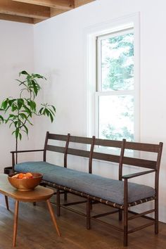 a wooden bench sitting in front of a window next to a bowl of fruit on a table