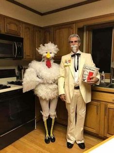 an old man and woman dressed up as chickens in the kitchen, one is holding a magazine