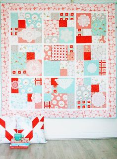 a quilted wall hanging on the wall next to a red and white basket filled with flowers