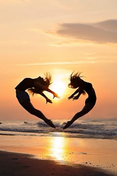 two people jumping into the air with their arms in the shape of a heart at sunset